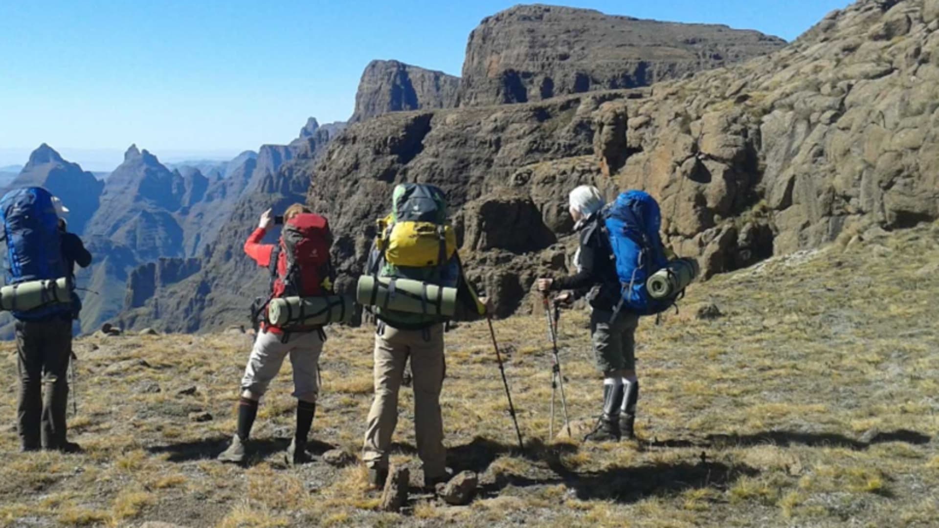 Vier Personen beim Trekking auf dem Hochplateau der Drakensberge blicken auf Schluchten und Felsmassive Südafrikas.
