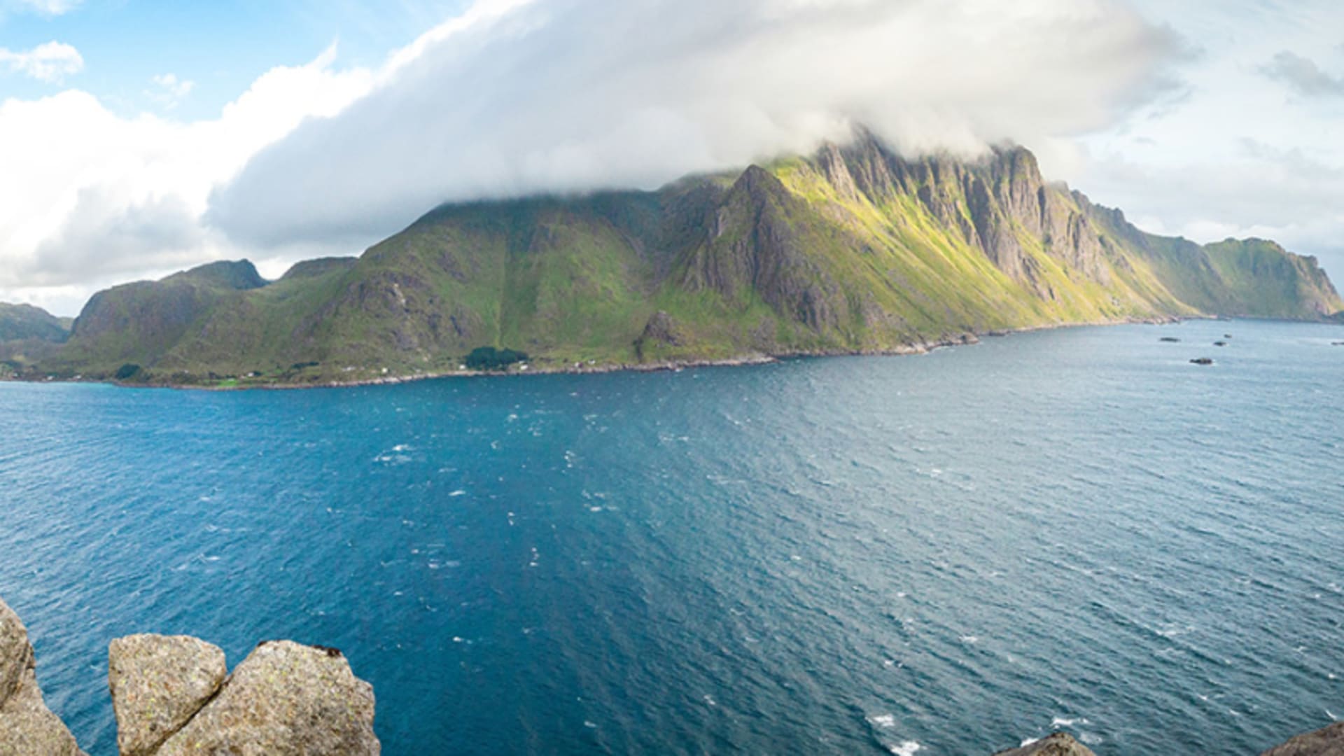 Trekking auf den Lofoten: Panoramablick von erhöhtem Gipfelstandpunkt über eine tiefblaue Meeresbucht mit Halbinsel