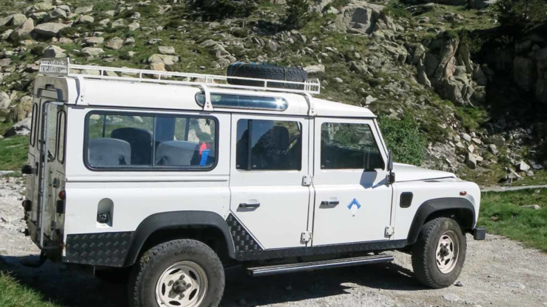Trekking in den Pyrenäen: Weißer Land Rover Defender als Wandertaxi auf einem Schotterweg bei Espot im Sommer.