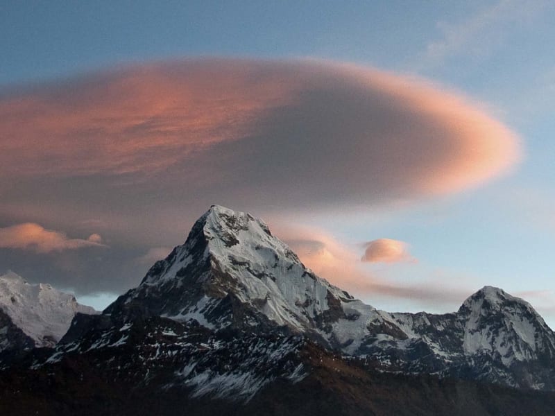 Trekking in hochalpinen Bergen: spitzer Gipfel mit Schnee und lentikularer Wolke in orange-rosa Farbtönen.