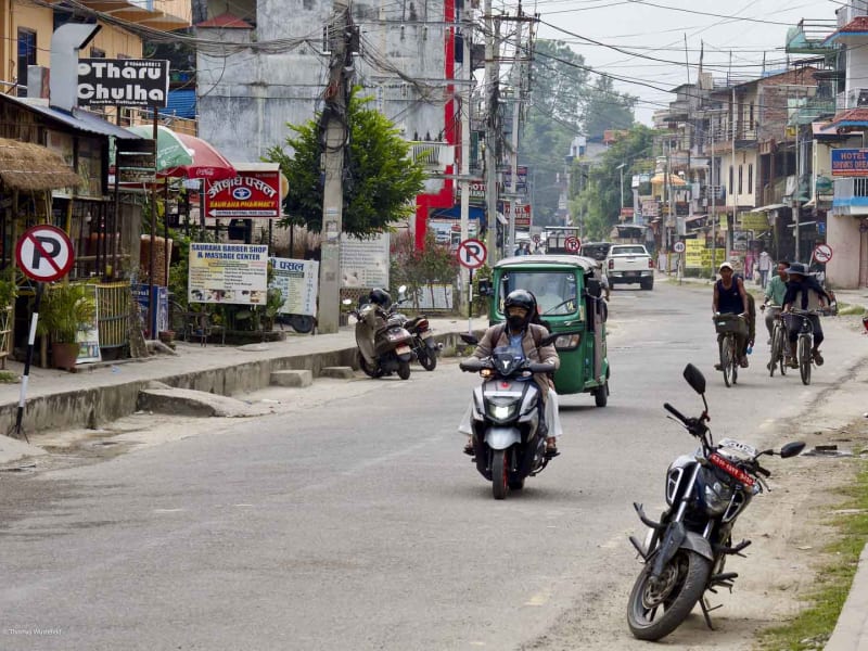 Trekking-Basis Sauraha in Chitwan, Südnepal: belebte Hauptstraße mit Motorrollern, Rikschas und Läden in Devanagari-Schrift.