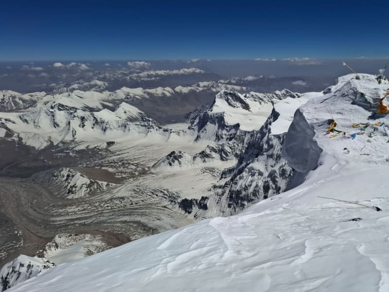 Bergtour auf den Muztagh Ata: felsiger Gipfelaufbau mit Gebetsfahnen, Schneestrukturen und Gletscherpanorama in China.