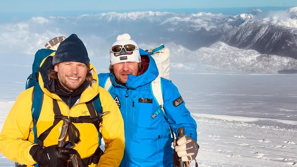 Bergtour mit Sebastian Ströbel: zwei Personen in Winterausrüstung vor schneebedeckter Gletscherlandschaft und Bergketten.