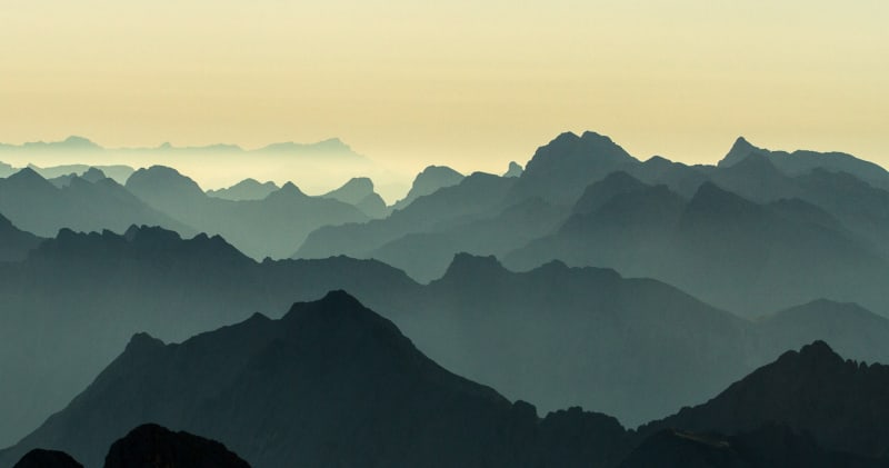 Hochtour in den Alpen: Panoramablick über mehrere gestaffelte Bergketten im Dämmerungslicht.