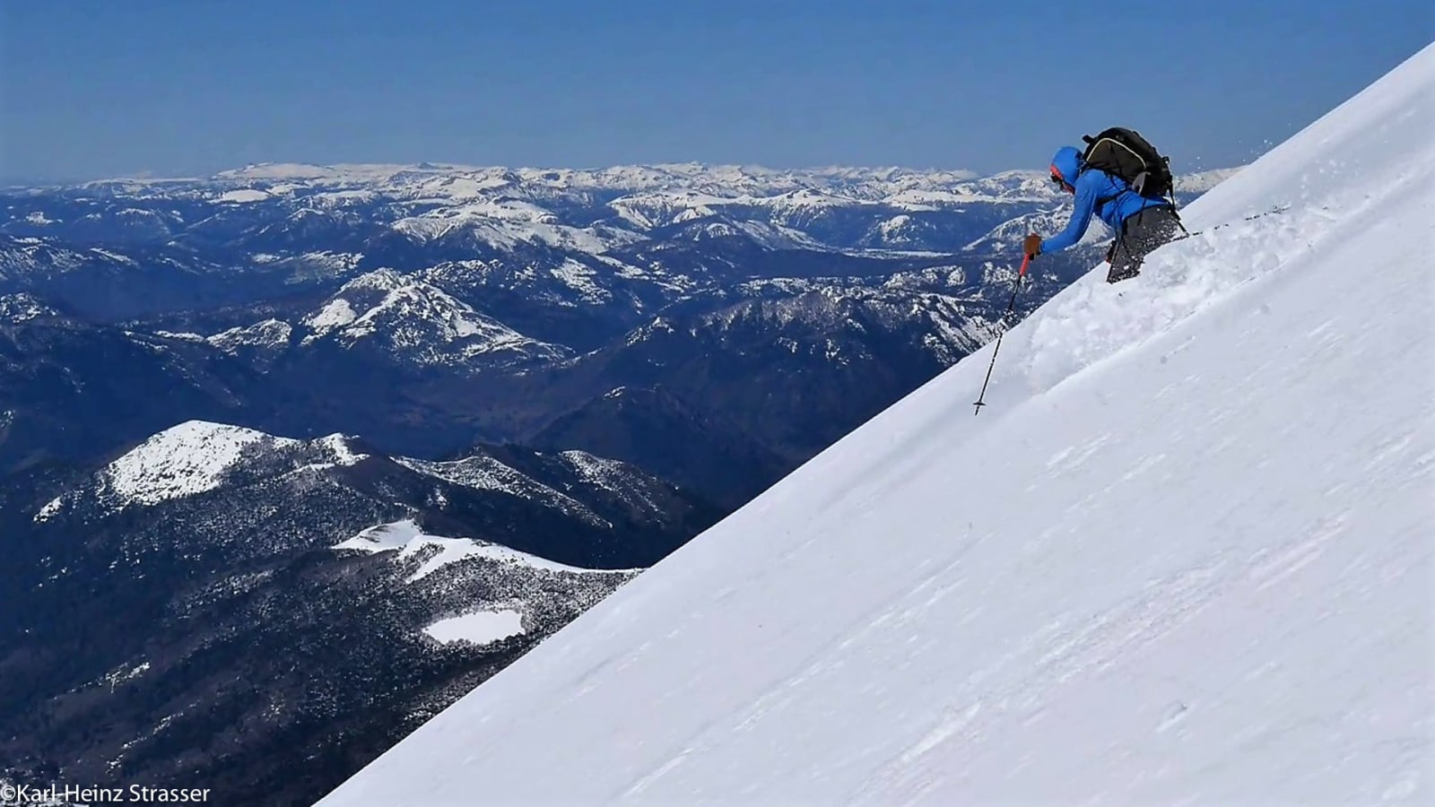 Bergtour am Abfahrtstraum: Bergsteiger mit blauer Jacke und Skistock steigt steil durch Tiefschnee