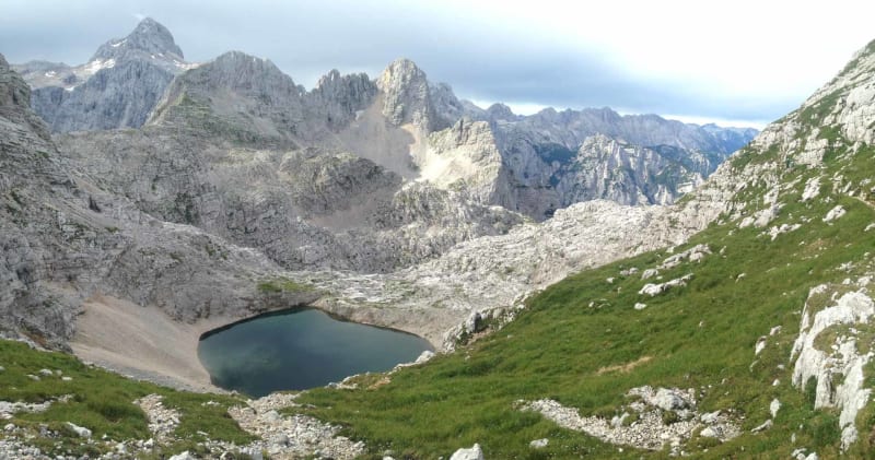 Bergtour in den slowenischen Bergen: Hochgebirgssee in einem Kalksteinkar mit Felsgipfeln im Hintergrund.