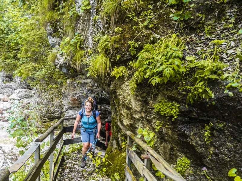 Bergwanderung in der Slizza Klamm: zwei Bergwanderer auf Holzsteg entlang türkisfarbenem Gebirgsfluss.