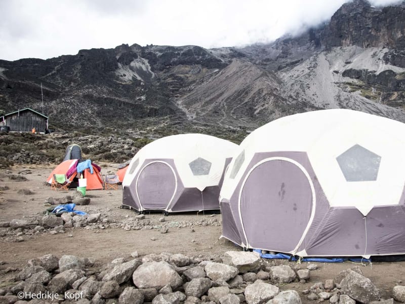 Expedition am Kilimanjaro: Kuppelzelte im Barranco Camp auf steinigem Plateau vor dunklem Felsmassiv.