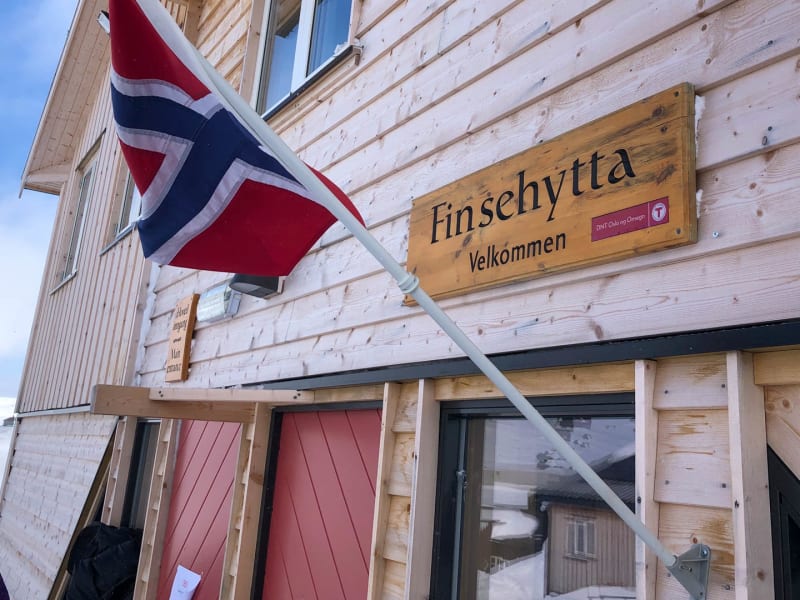 Expedition auf der Hardangervidda: Eingang der Finsehytta mit DNT-Logo und norwegischer Flagge im Winter.