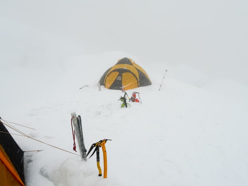 Expedition am Chopicalqui: Hochlager mit zwei gelb-schwarzen Kuppelzelten und Eispickeln bei starkem Schneefall im Weißout.