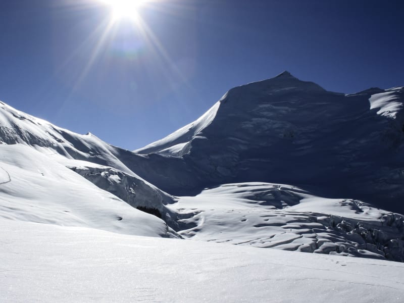 Expedition zum Verbindungsgrat am Himlung Himal: Spur im Schneefeld führt zu einem Hochpass unter blauem Himmel.