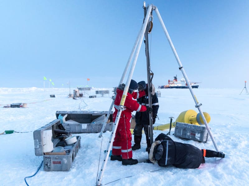 Expedition Mosaic: Drei Wissenschaftler arbeiten an einem Dreibein-Gestell bei Met City, gelbe Sonde und Eisbrecher Polarstern