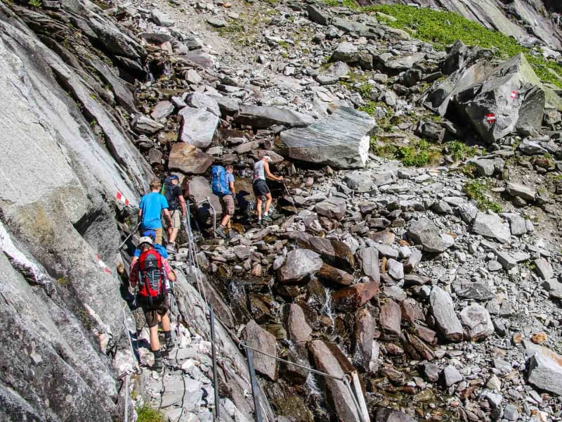 Hochtour am Anstieg zur Kürsinger Hütte: Vier Bergsteiger auf gesichertem Felsweg mit Stahlseilen und rot-weißer Wegmarkierung