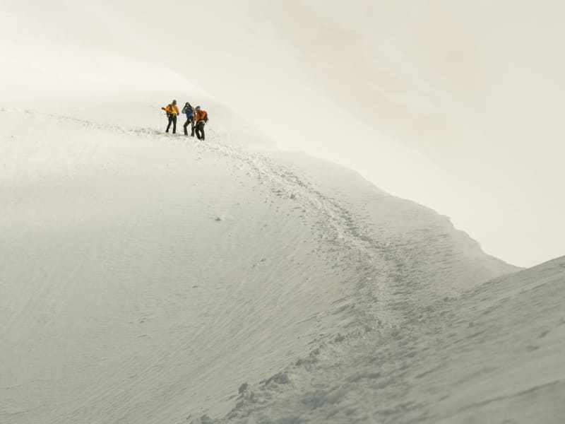 Drei Bergsteiger pausieren auf einem verschneiten Hang bei der Hochtour zur Jungfrau im Berner Oberland.