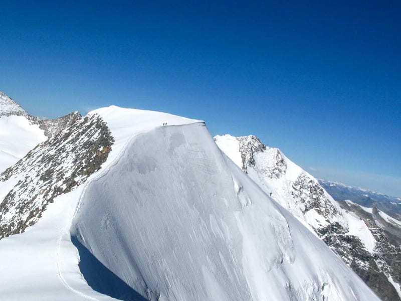 Hochtour Piz Palü: zwei Bergsteiger auf dem Schneegrat mit markanter Wechte und schneebedecktem Gipfel im Hintergrund.