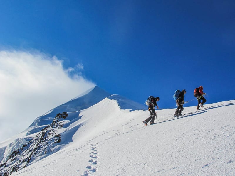 Hochtour Piz Palü: drei Bergsteiger in Seilschaft mit Steigeisen und Eispickel beim Aufstieg über den Schneehang.