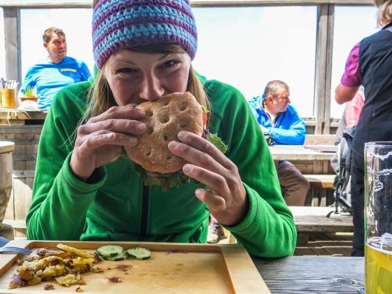 Klettern in den Dolomiten: Kletterin bei der Brotzeit auf der Plattkofel-Hüttenterrasse mit Wanderstöcken im Hintergrund.
