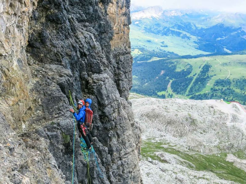 Zwei Kletterer am Standplatz einer senkrechten Kalkfelswand am Bosseekofel in den Dolomiten mit Blick ins Tal.