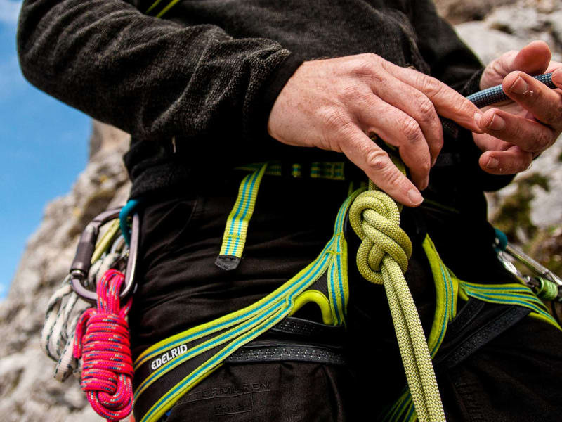 Klettern am Gardasee: Person bindet Achterknoten in Edelrid-Klettergurt mit Karabinern, Felsgrat im Hintergrund.