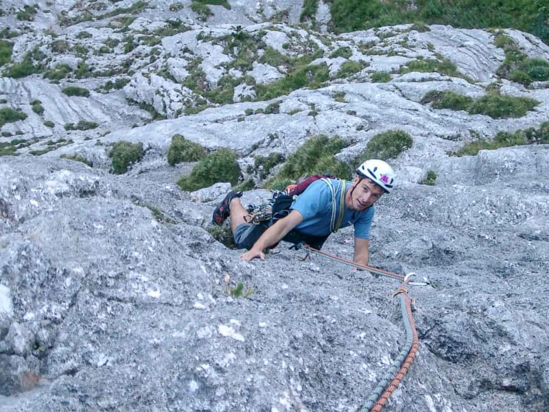 Kletterer mit weißem Helm und Rucksack steigt an geneigter Kalksteinplatte in den Allgäuer Alpen auf, Seil am Haken.
