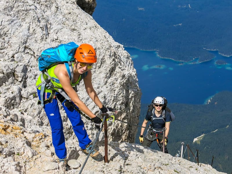 Klettersteig im Höllental: zwei Klettersteiggeher an Metallbolzen mit Tiefblick auf den See.