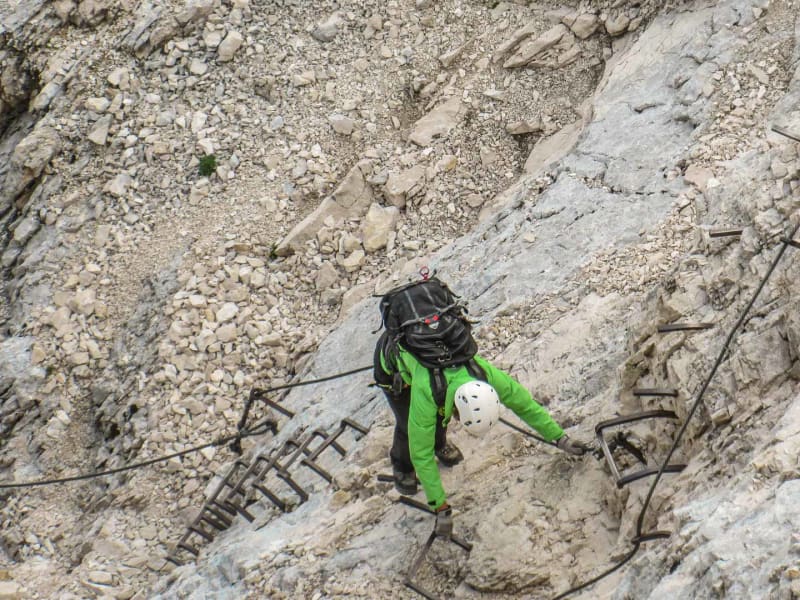 Klettersteiggeher klettert an senkrechter Kalkfelswand der Alpspitze an Metallbügeln und Stahlseil.