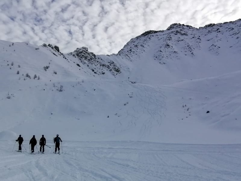 Vier Skitourengeher von hinten beim Aufstieg am Mont de Flassin auf verschneitem Kesselgelände im Winter.
