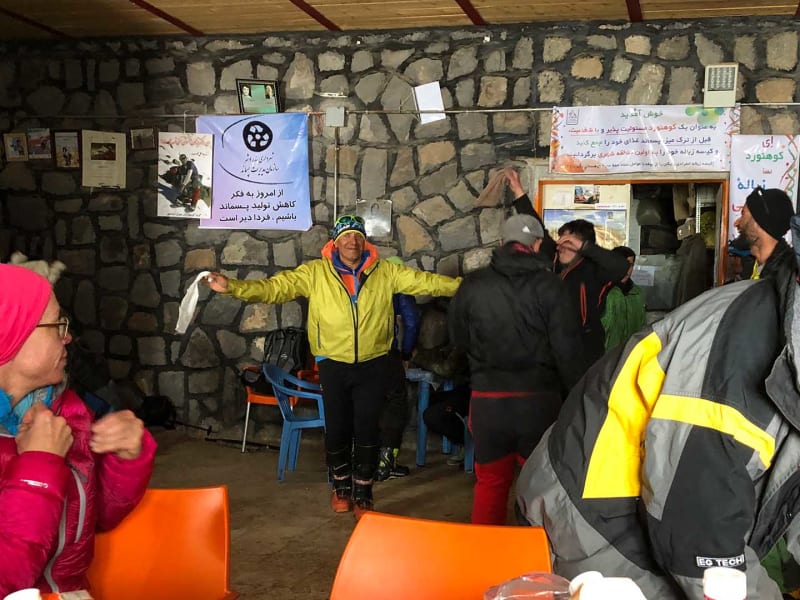 Skitourengeher feiern den Gipfelerfolg am Damavand in einer Schutzhütte mit Natursteinwänden im Iran.