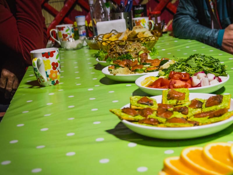 Skitour in Kirgistan: Gedeckter Tisch in einer Jurte mit Fladenbrot, Fleisch, Salat und Brot als traditionelle Verpflegung.