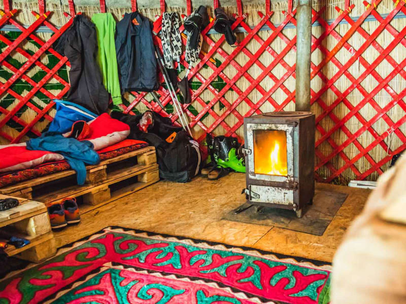 Skitour in Kirgistan: Jurteninneres mit Holzofen, Skischuhen und Winterausrüstung der Skitourengeher.