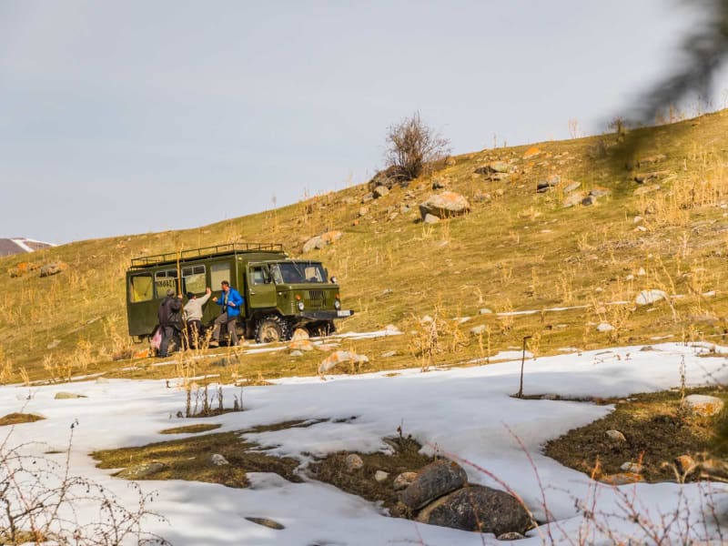 Skitour Kirgistan: Drei Personen beladen einen militärgrünen GAZ-66-Truck am Yurten-Camp vor schneebedeckten Bergen.