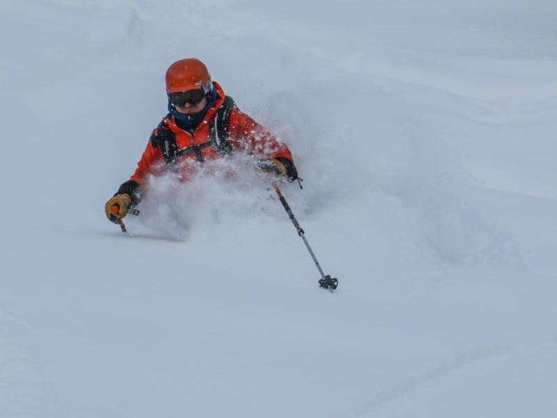 Skitourengeher fährt in Sibirien durch tiefen Pulverschnee ab, eine Schneewolke umhüllt den Unterkörper.