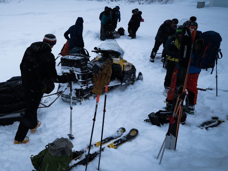 Gruppe von Skitourengehern belädt ein Schneemobil vor der Hütte Luzhba in Sibirien bei Schneefall.