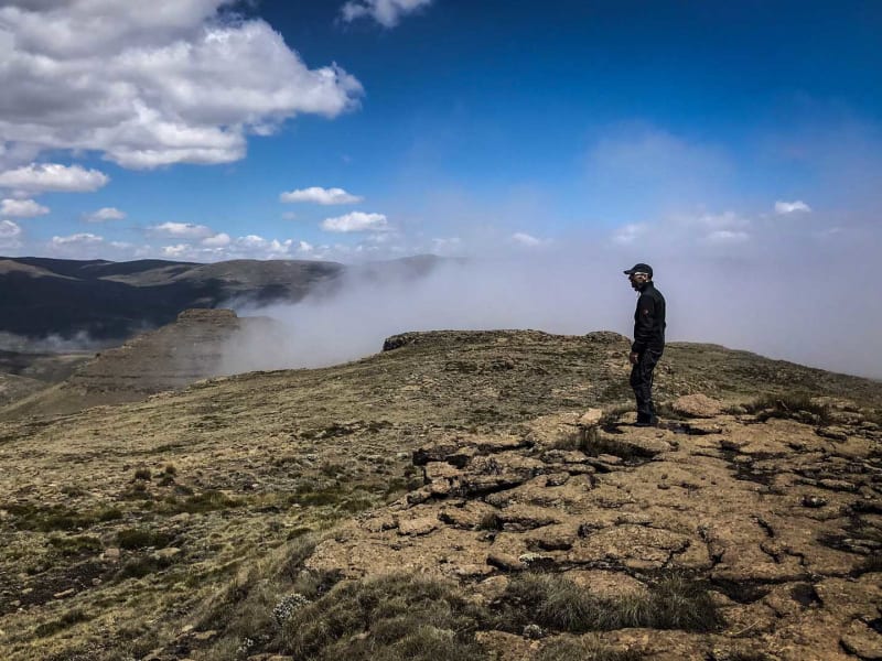 Trekking in den Drakensbergen Südafrika: Person steht auf felsigem Plateau-Rand und blickt auf markante Felstürme