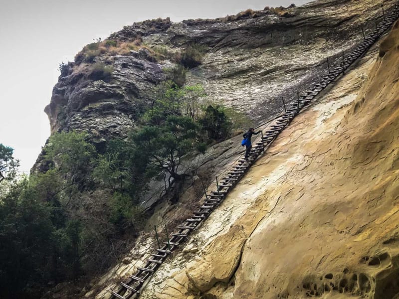 Trekking am Holkrans: ein Trekker in blauer Jacke steigt eine mehrteilige Holzleiter an der Sandsteinwand im Golden Gate