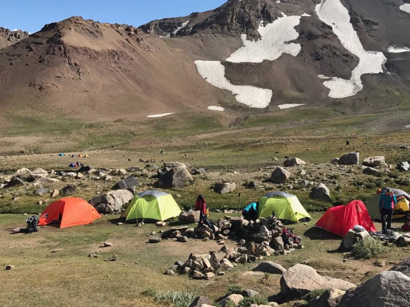 Trekking im Iran: Kleines Basecamp mit fünf Expeditionszelten auf steinigem Plateau vor dunklem Vulkankegel