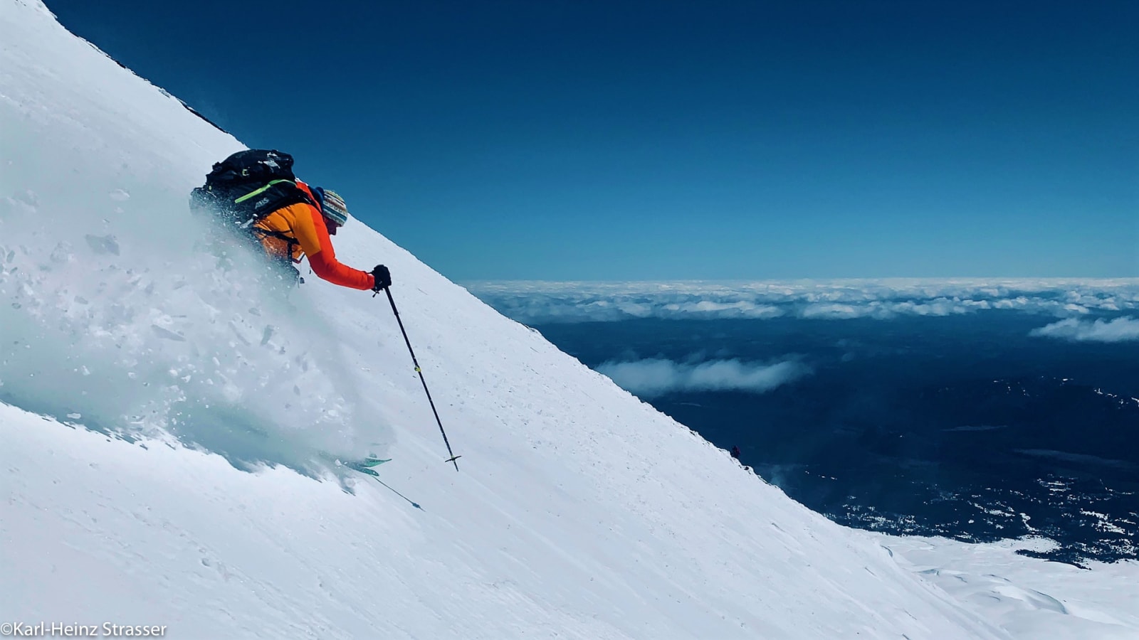 Bergtour Abfahrtsrausch: Skifahrer in orangefarbener Jacke fährt einen steilen, unverspurten Pulverschneehang ab