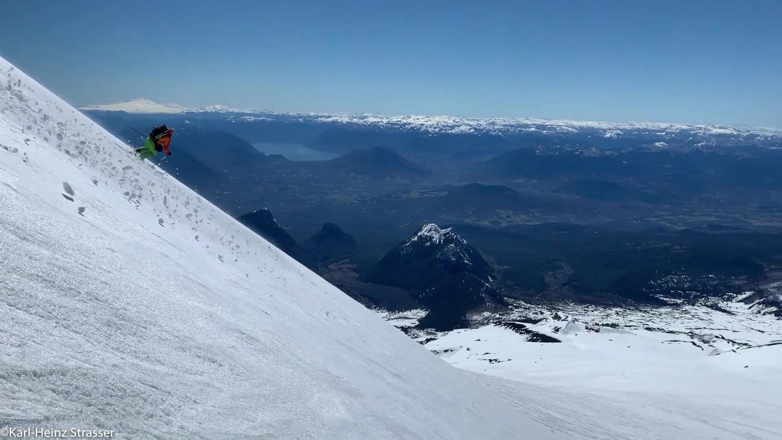 Bergtour am Genial-Hang: Skifahrer in grüner Jacke fährt steilen Schneehang ab, im Hintergrund Felsgipfel
