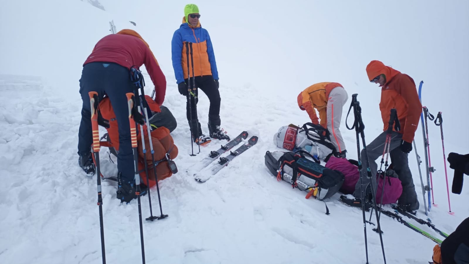 Vier Bergsteiger pausieren mit Skitouren-Ausrüstung auf verschneiter Fläche am Muztagh Ata bei dichtem Nebel.