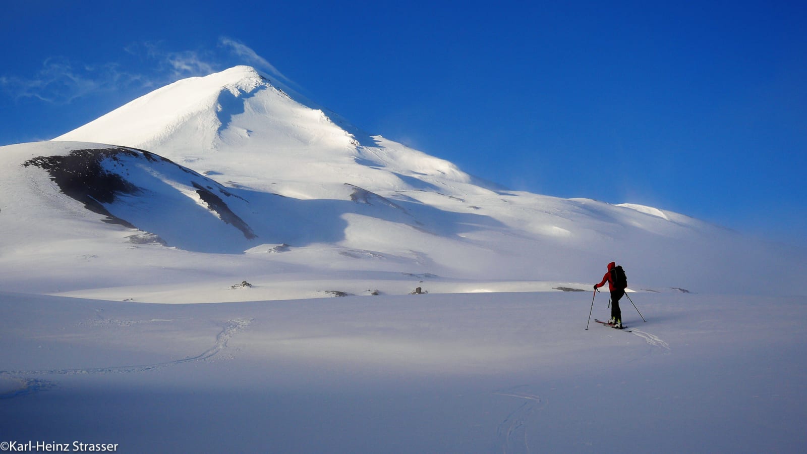 Bergtour Der Weg ist das Ziel: Skiläufer mit Aufstiegsfellen quert ein weites Schneeplateau vor massivem verschneitem Gipfel