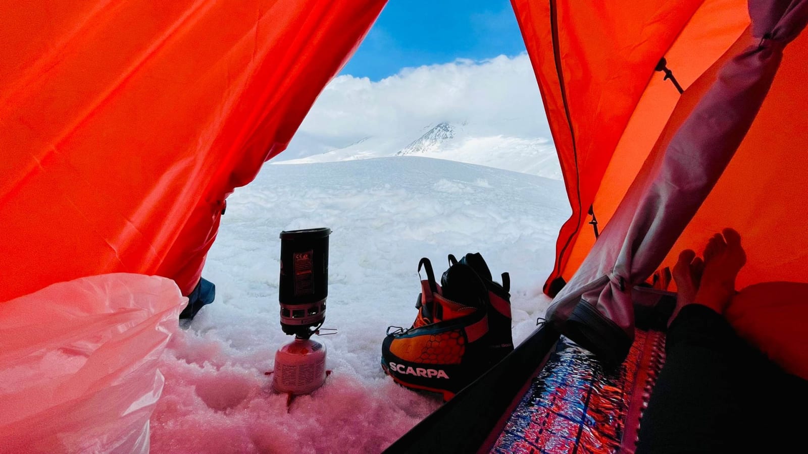 Bergtour am Pik Lenin: Blick aus orangefarbenem Hochlagerzelt auf verschneiten Gletscher und Gipfel.