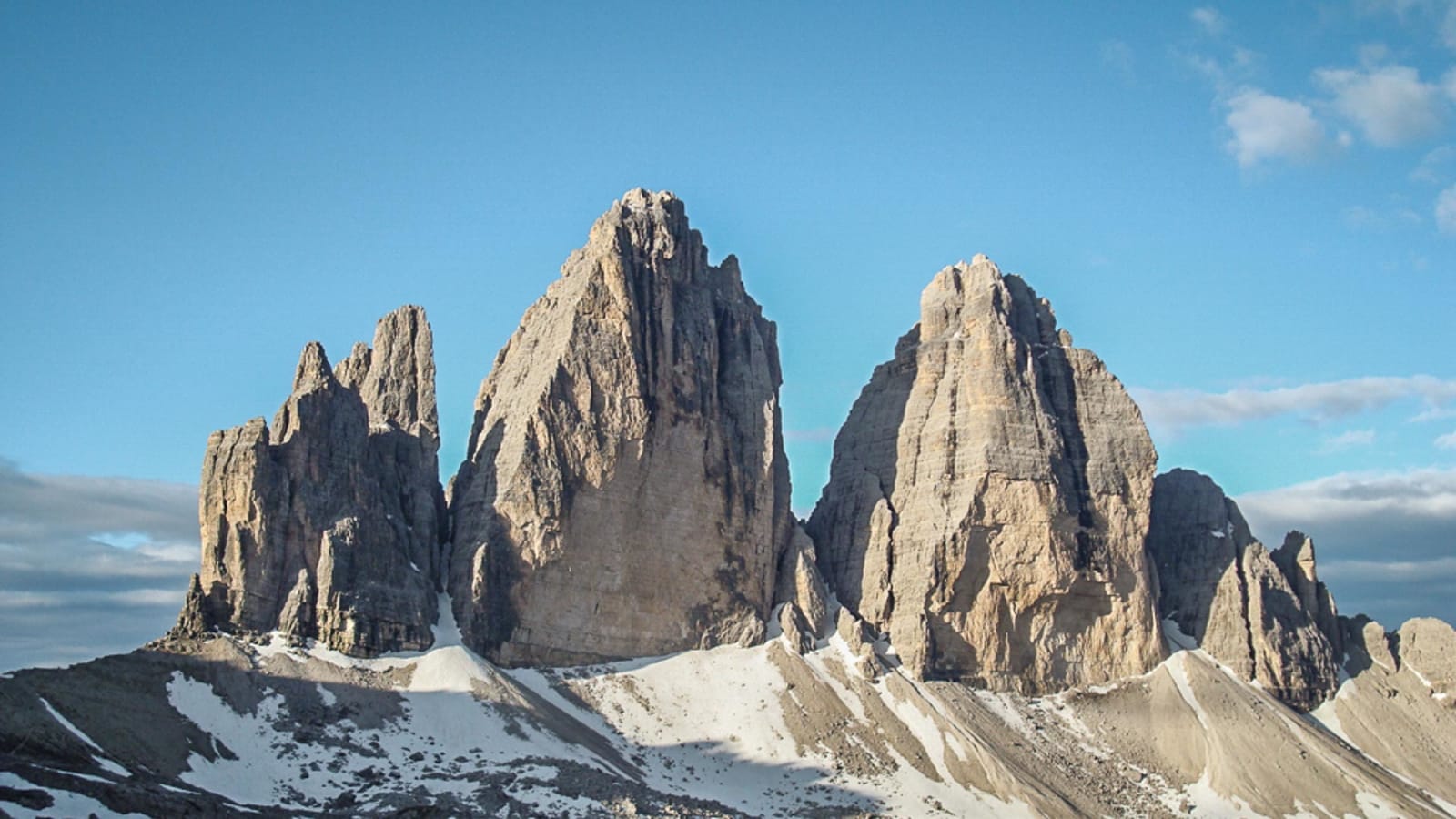Bergwanderung zu den Drei Zinnen: Frontalansicht der drei Felstürme aus Dolomitgestein über einem felsigen Hochplateau