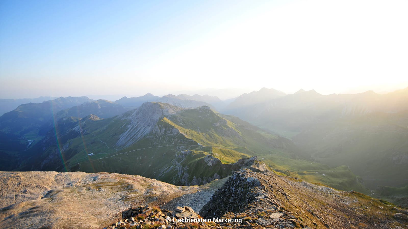 Bergwanderung in Liechtenstein: Blick vom felsigen Grat über alpine Bergketten im Abendlicht.