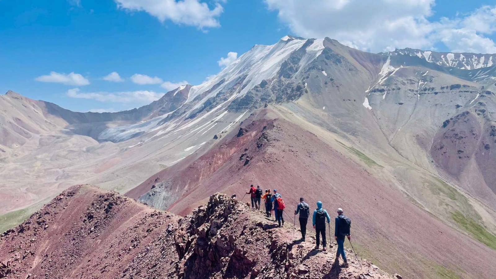 Expedition Pik Lenin: Gruppe von sieben Höhenbergsteigern auf felsigem Grat mit Schneefeldern im Hintergrund.