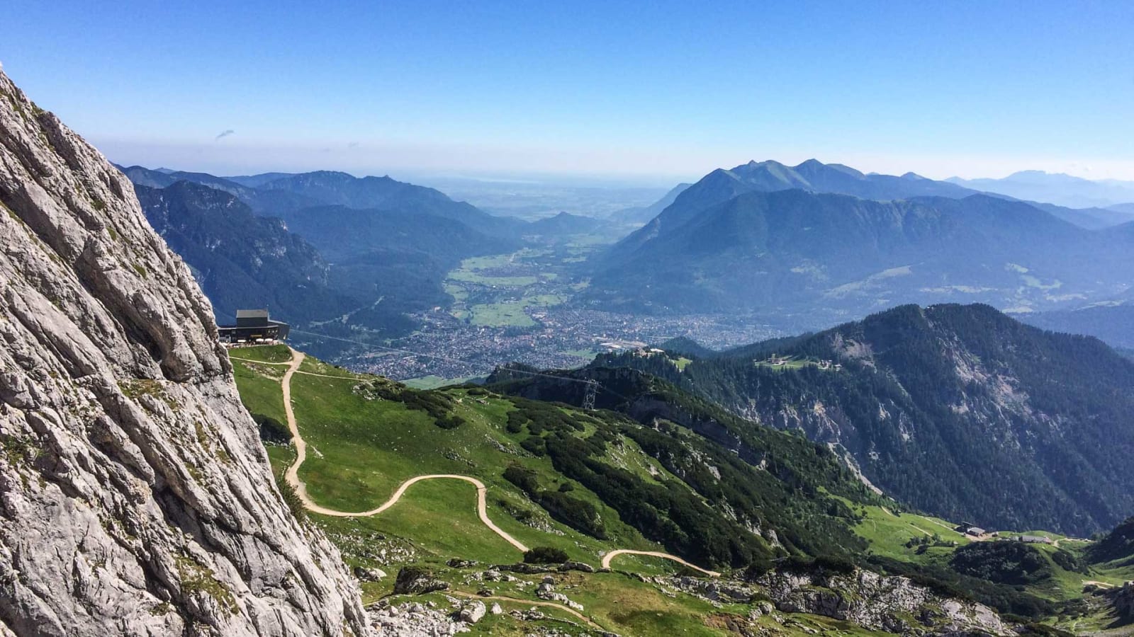 Klettersteig an der Alpspitze mit Blick auf Garmisch-Partenkirchen im Talboden und Bergstation an der Kalkfelswand.