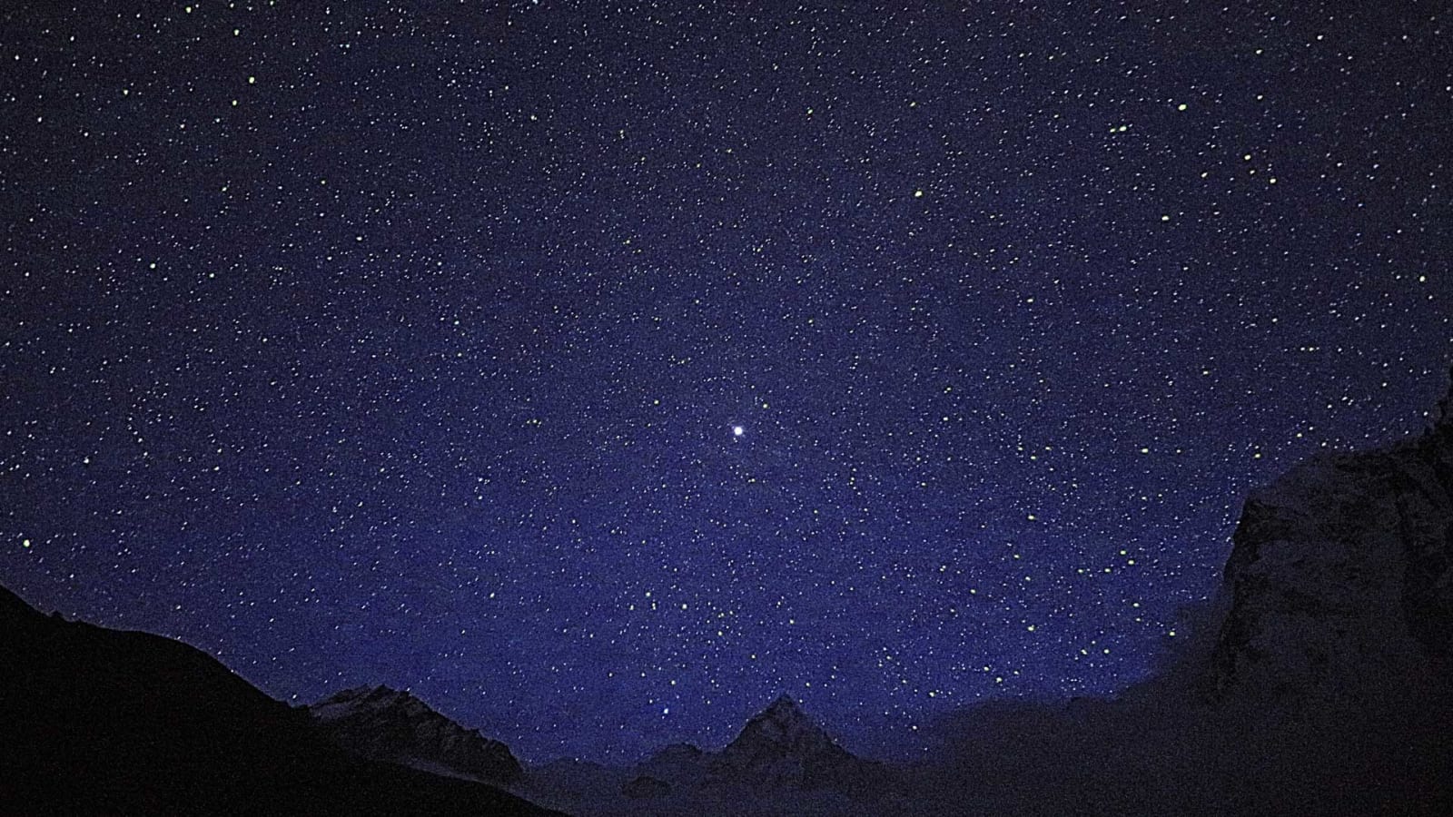 Trekking in Nepal: Nächtlicher Sternenhimmel über Himalaya-Bergsilhouetten mit spitzem Gipfel im Vordergrund.