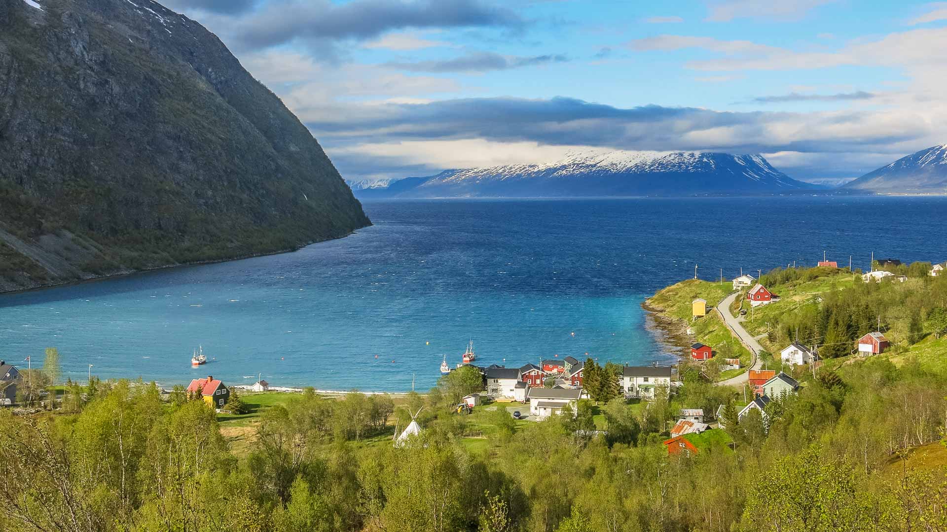 Bergwanderung in Norwegen: Blick auf die Fjordbucht von Koppangen mit Küstenort und schneebedeckten Bergen.