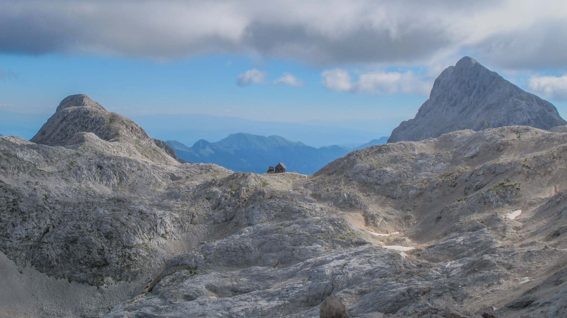Bergwanderung über ein hochalpines Kalksteinplateau in Slowenien mit Berghütte zwischen zwei Felsgipfeln.
