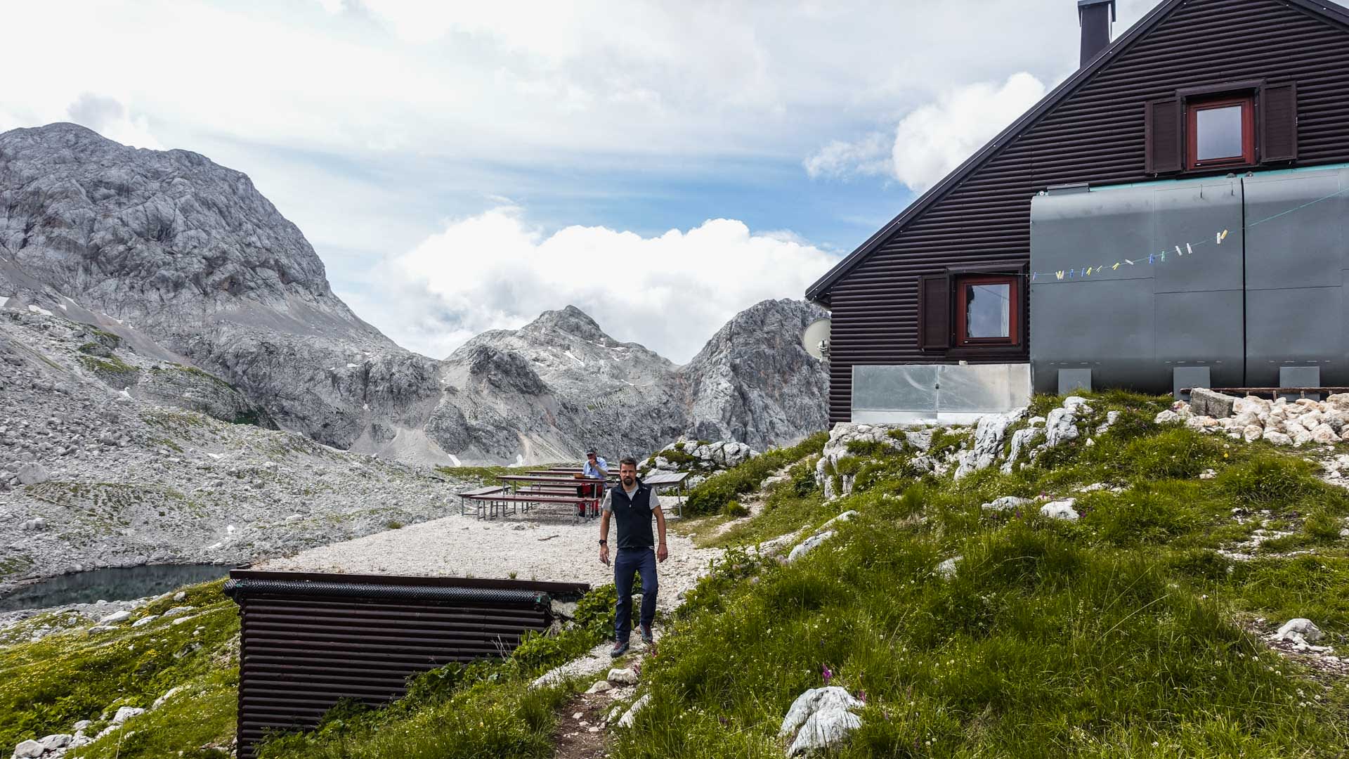Bergwanderer macht Pause an einer Berghütte mit Außenterrasse vor Kalkfelsbergen in den Julischen Alpen.