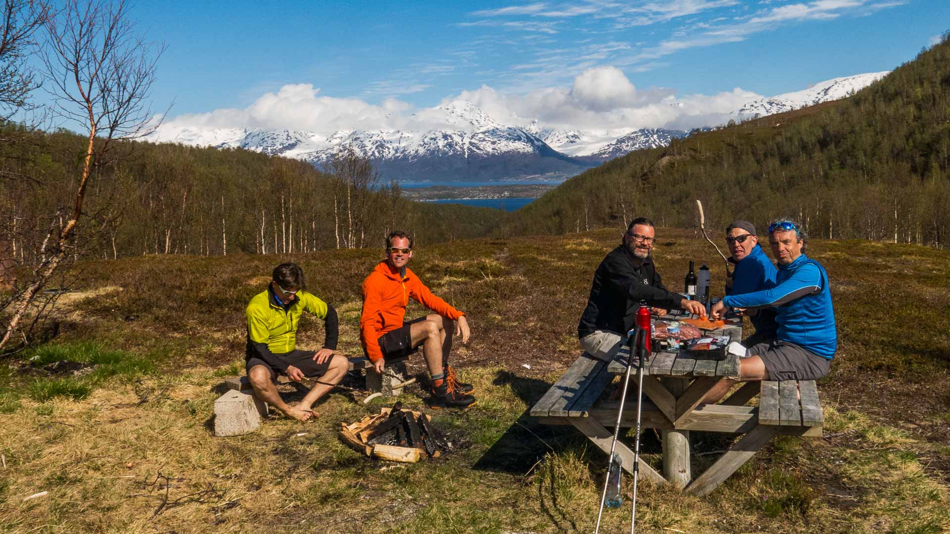 Vier Bergwanderer machen eine Pause am Lyngenfjord mit Blick auf schneebedeckte Gipfel in Norwegen.